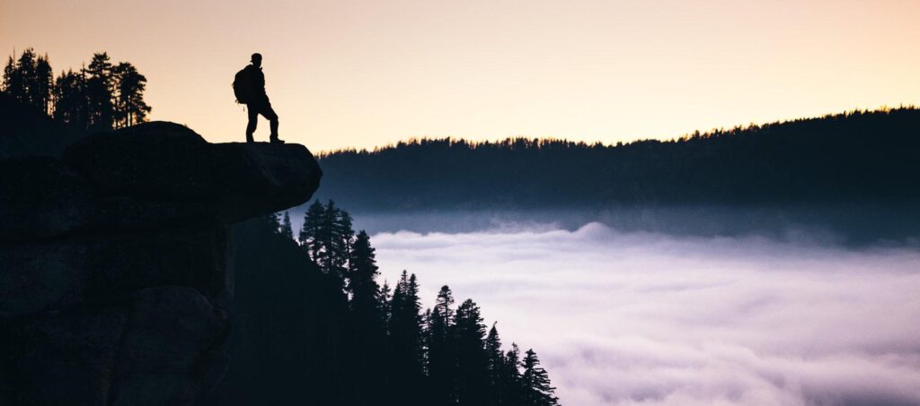 man standing at the edge of a cliff contemplating self improvement challenges