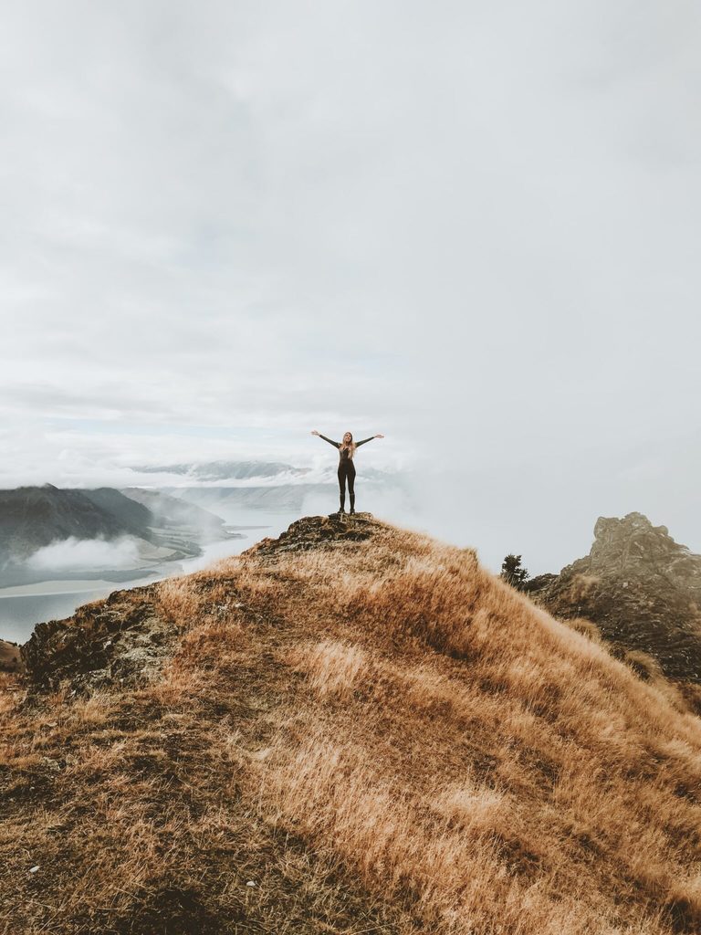 woman standing on top of hill with arms open